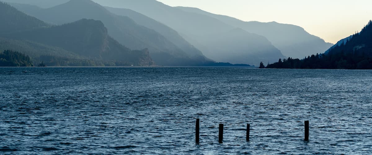 A calm lake with mountains in the background and wooden posts in the water.