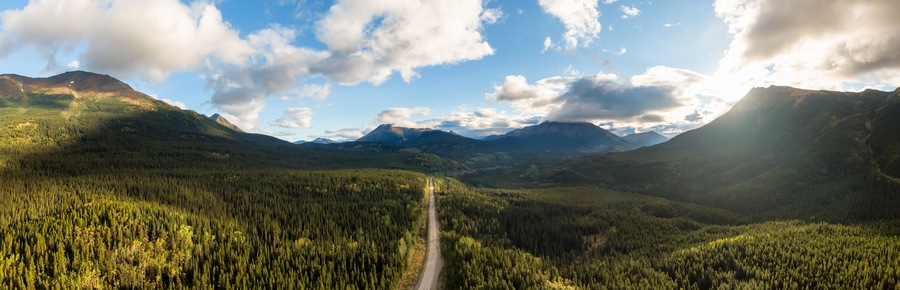 Beautiful View of Scenic Road surrounded by Lush Forest Valley and Mountains at Sunrise in Canadian Nature. Aerial Drone Shot. Taken near Stewart-Cassiar Highway, Northern British Columbia, Canada.