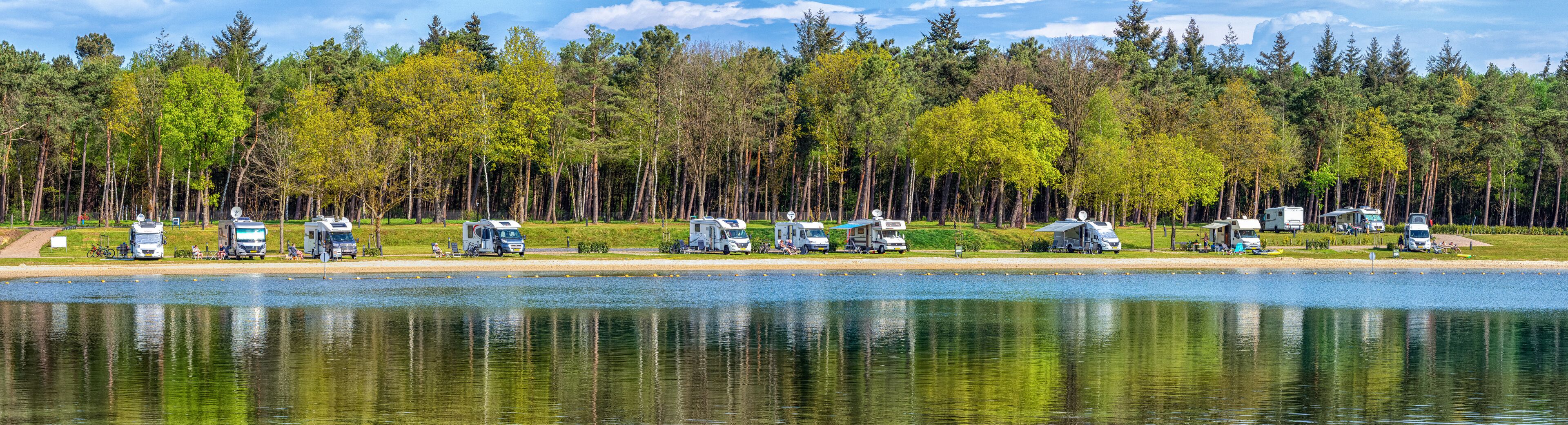 A lakeside campsite with RVs parked along the shore, surrounded by dense forest.