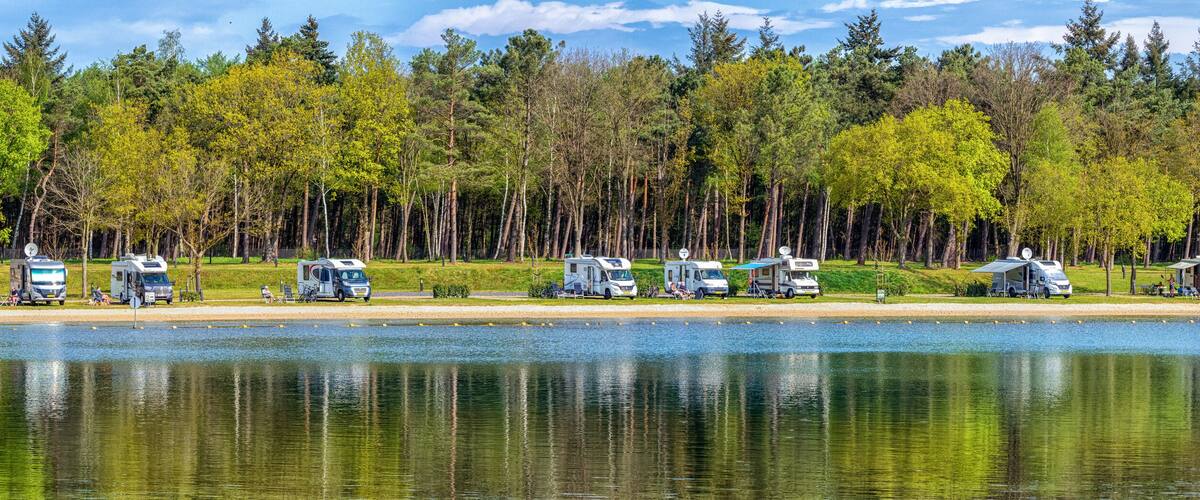 A lakeside campsite with RVs parked along the shore, surrounded by dense forest.