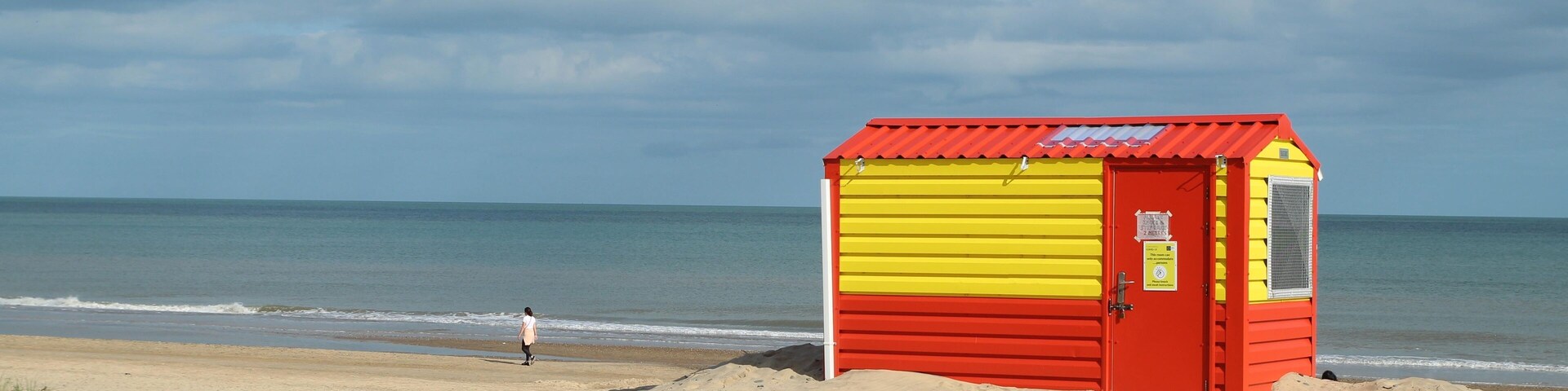 Orange and yellow lifeguard hut on Brittas Bay beach, County Wicklow, Ireland with overcast sky backdrop