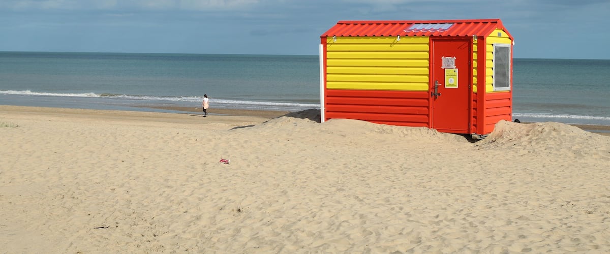 A beach with a red and yellow lifeguard hut near the water.
