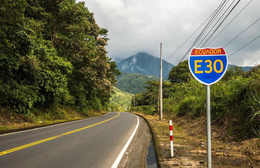 Road sign on an empty jungle street in Ecuador on the way from Banos to Puyo which is popular tourist bicycle trail. Blue and red sign with road number and country name in yellow.