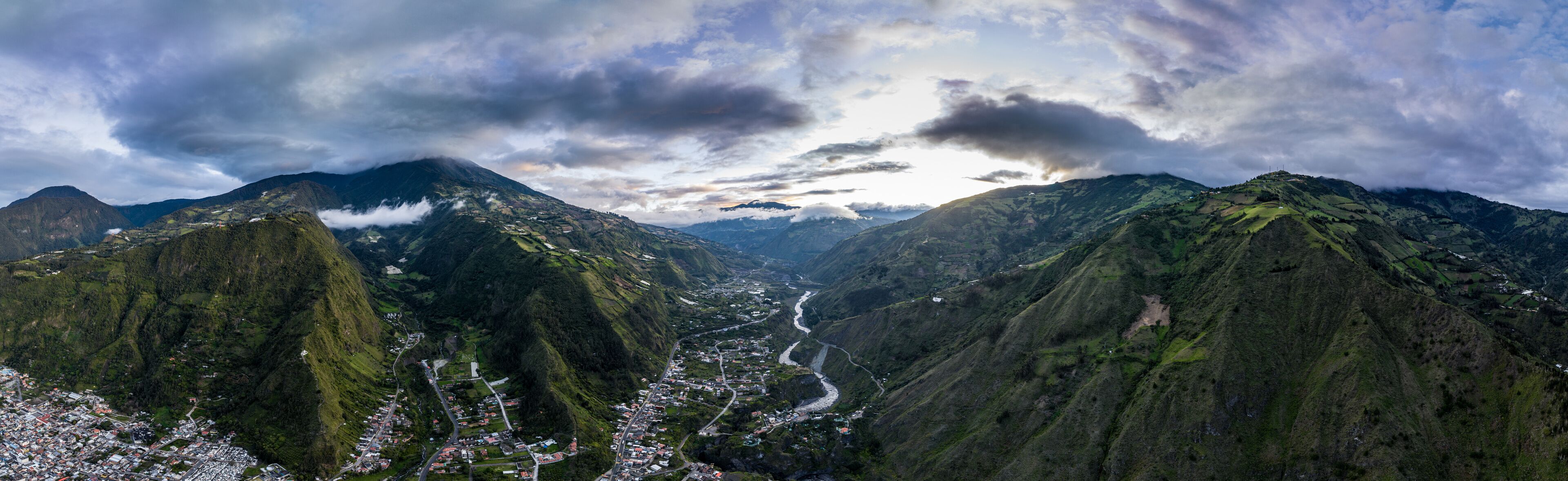 A mountainous landscape with a river winding through a valley, surrounded by lush greenery and a small town.