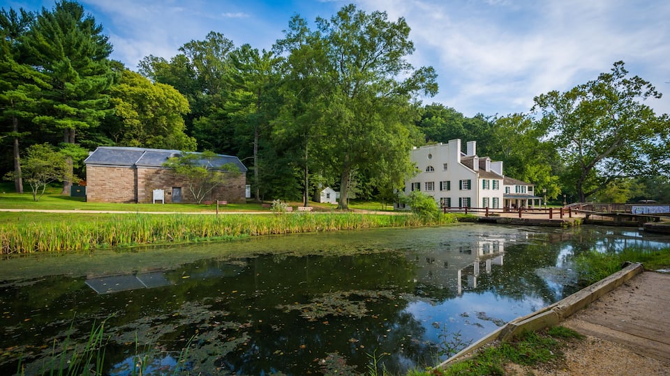 A serene riverside with a wooden dock, a brick building, and a white house with a chimney.