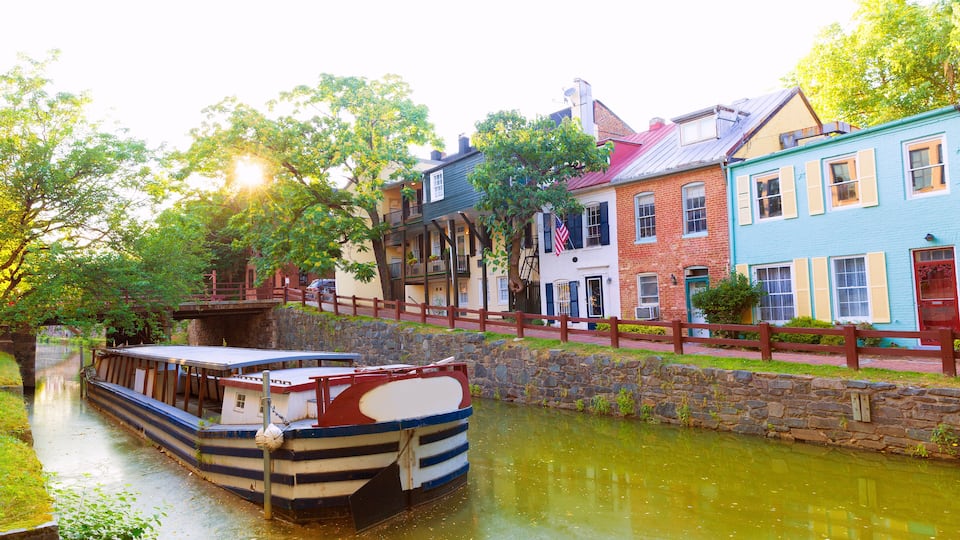 A narrow canal with a rowboat docked on the left, surrounded by historic buildings with colorful facades and a stone wall.