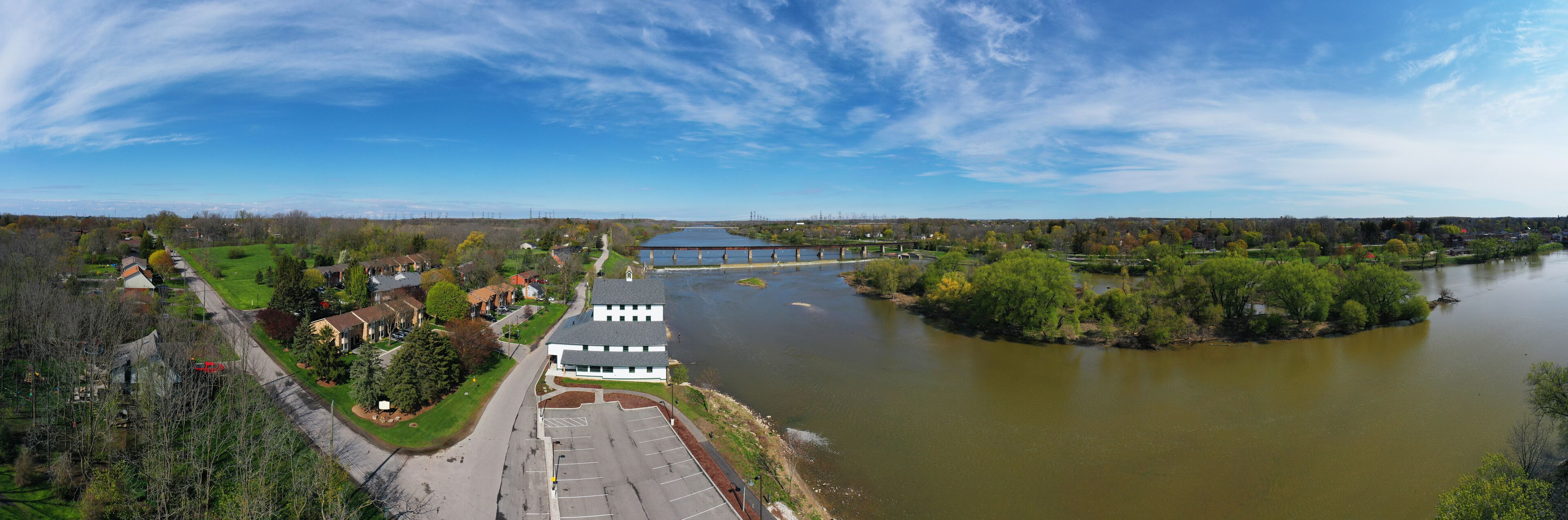 A river with a bridge, a parking lot, and a building with a green lawn.