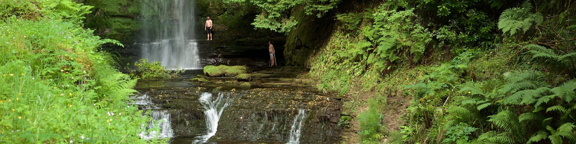 A waterfall in a forested area with a person standing at the base.