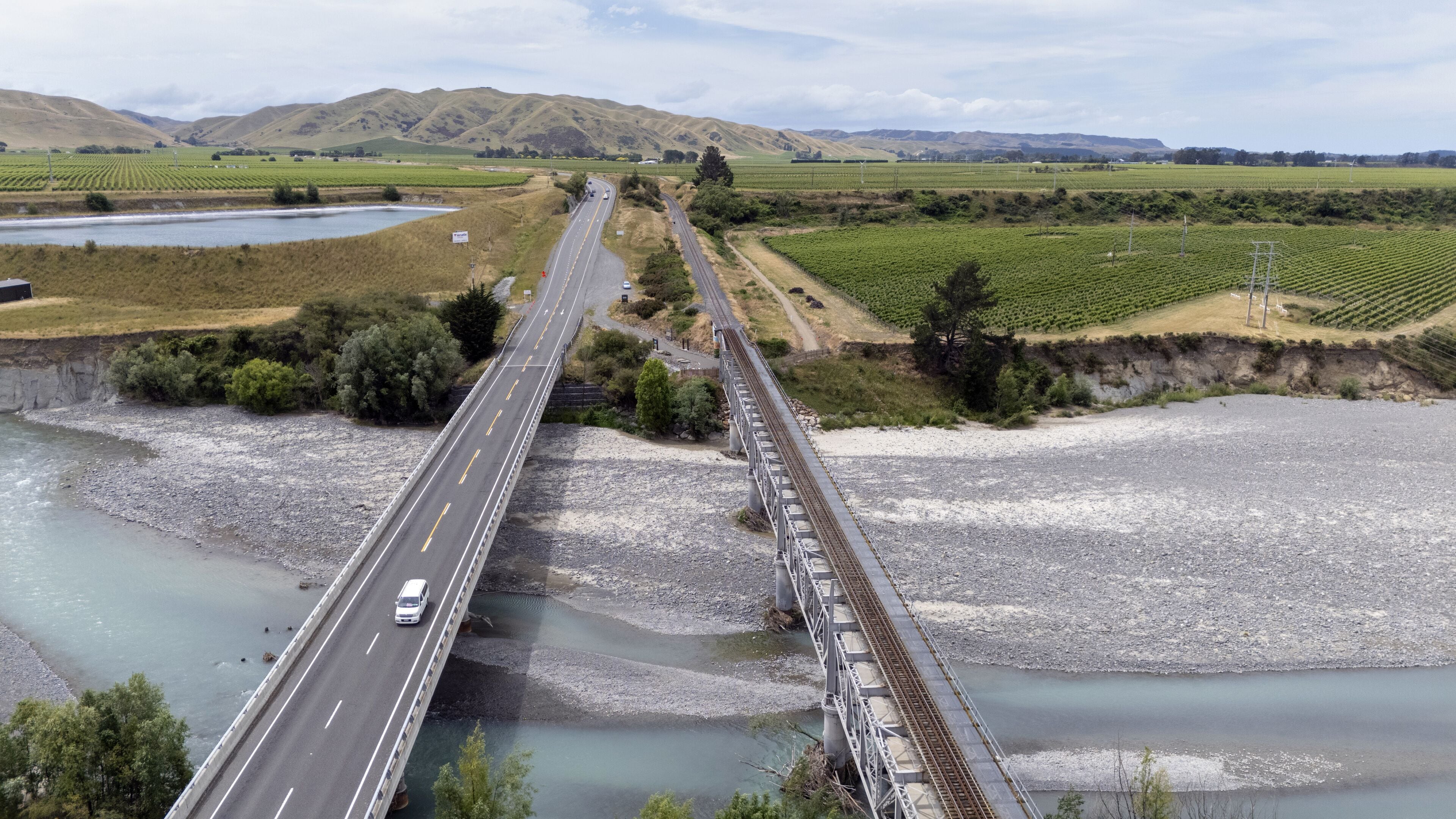 A bridge over a river with a road, surrounded by fields and hills.