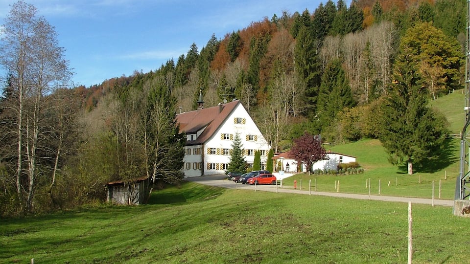 A white house with a brown roof surrounded by a green field and trees.