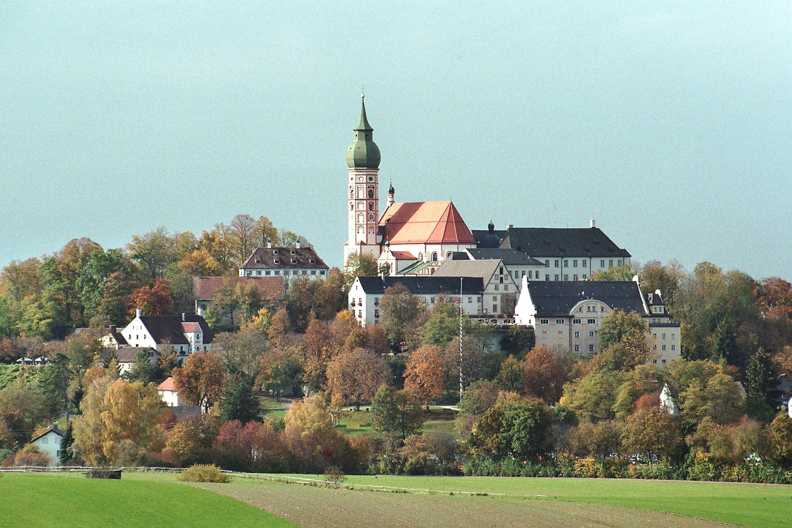 A historic building with a prominent tower, surrounded by autumn-colored trees and a green field.