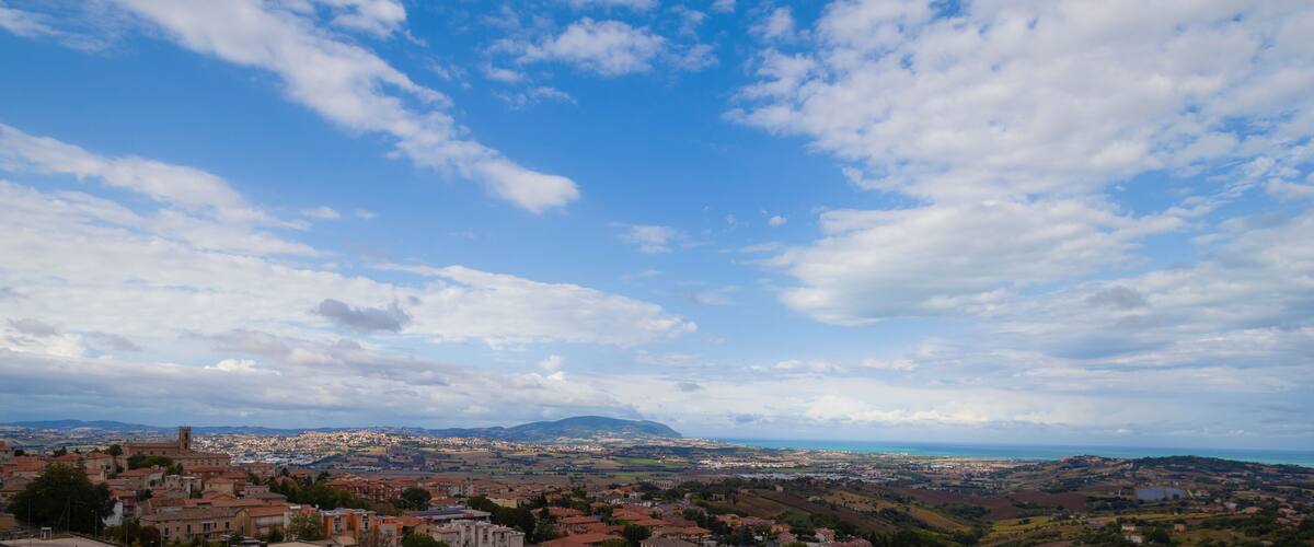 A coastal town with historic buildings, a prominent church, and a distant mountain range under a partly cloudy sky.