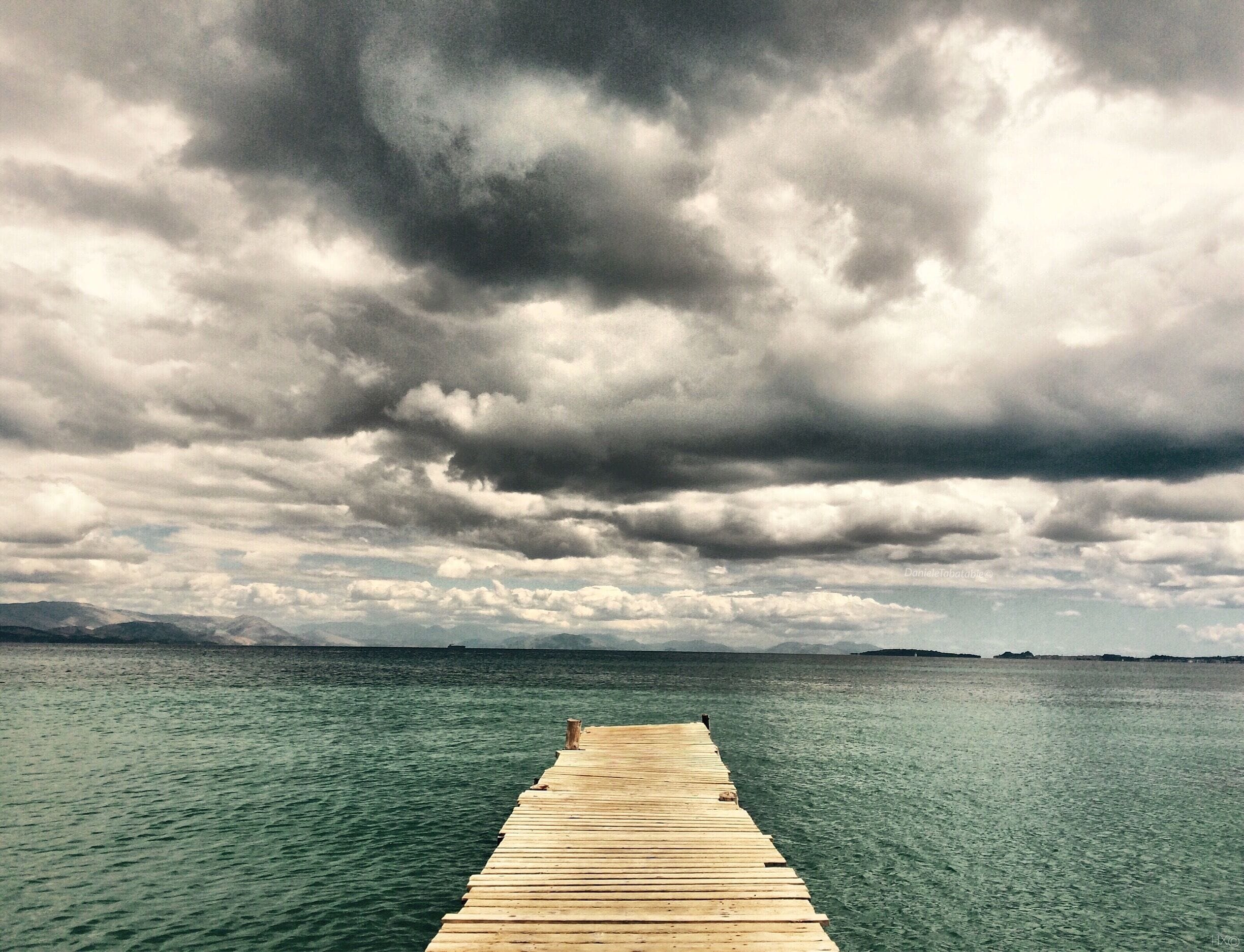 A wooden pier extending into a calm body of water under a cloudy sky.