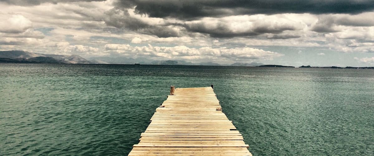 A wooden pier extending into a calm body of water under a cloudy sky.