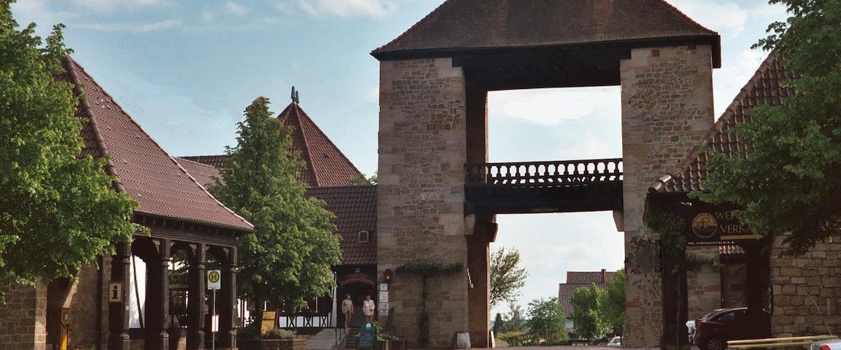 A stone archway with a sign reading "WATER VERHAUS" in front of a building with a tiled roof.