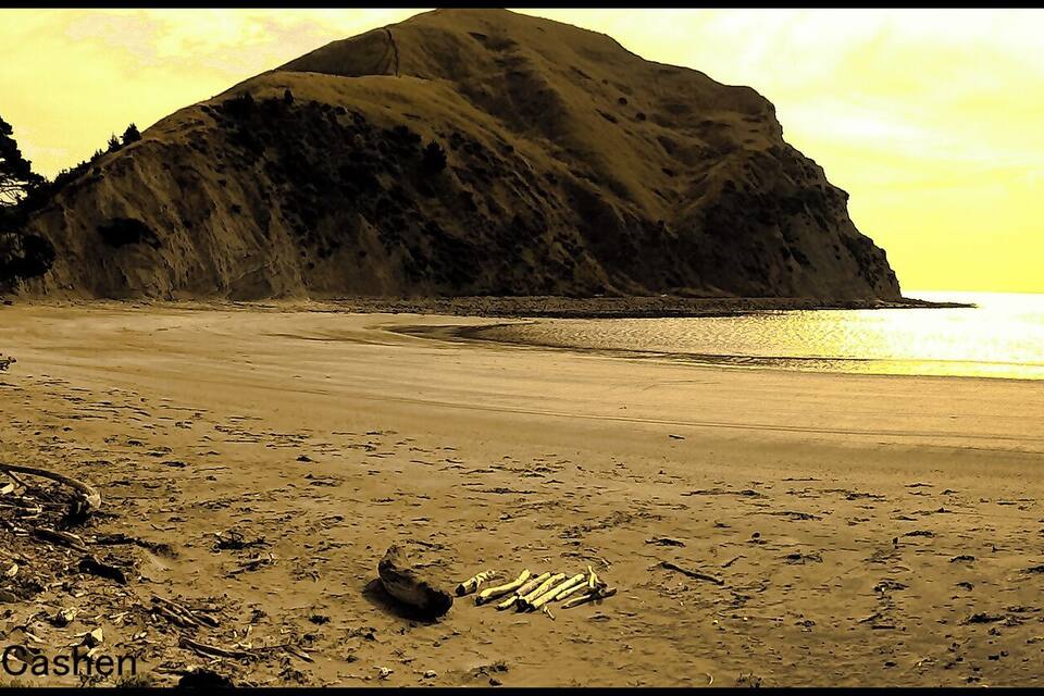 A beach with a large rock formation and mountains in the background.