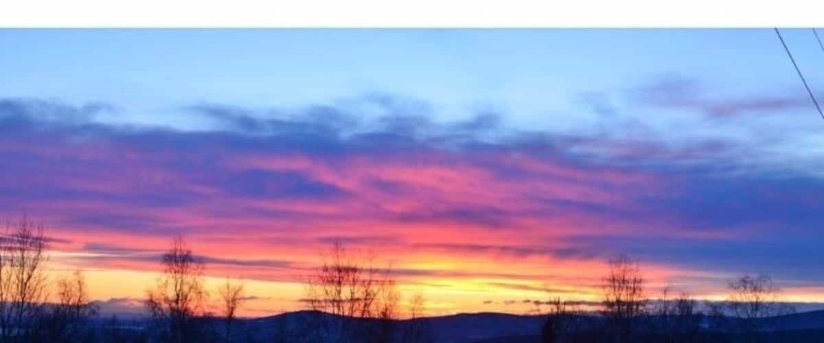 A sunset over a snowy landscape with bare trees and a distant cabin.