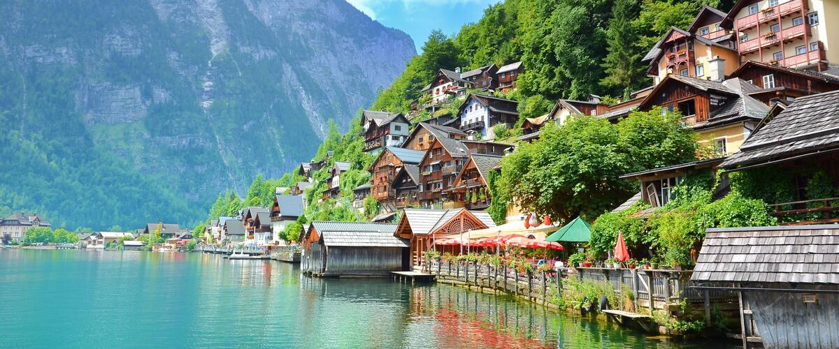 A lakeside village with wooden houses, a dock, and a mountain backdrop.