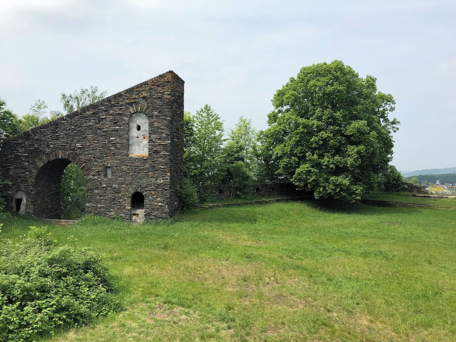 An old stone building with arched doorways and a large tree in the foreground.
