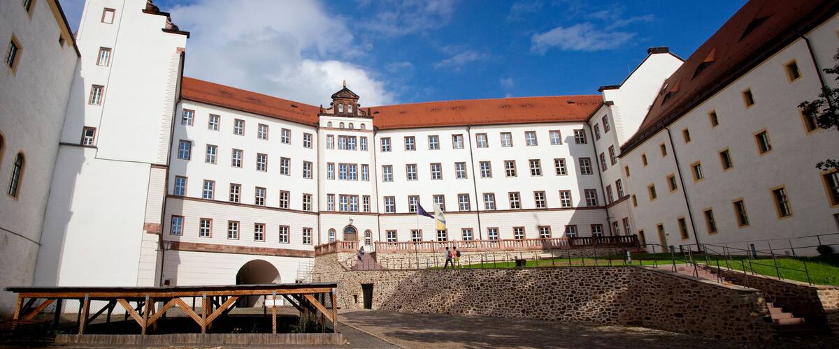 A historic building with a central courtyard, stone walls, and a flagpole.