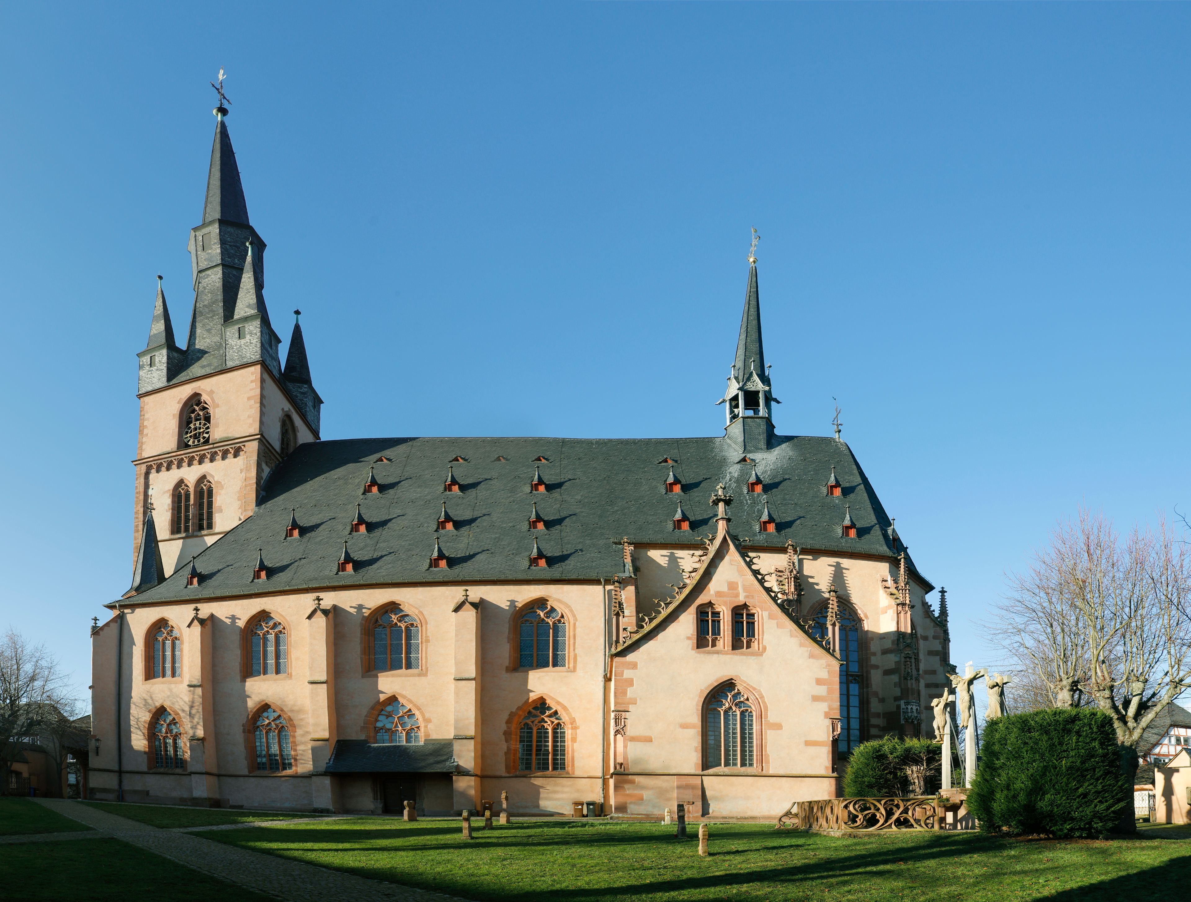 A church with a large central tower and two smaller towers, surrounded by a well-maintained lawn and a statue.