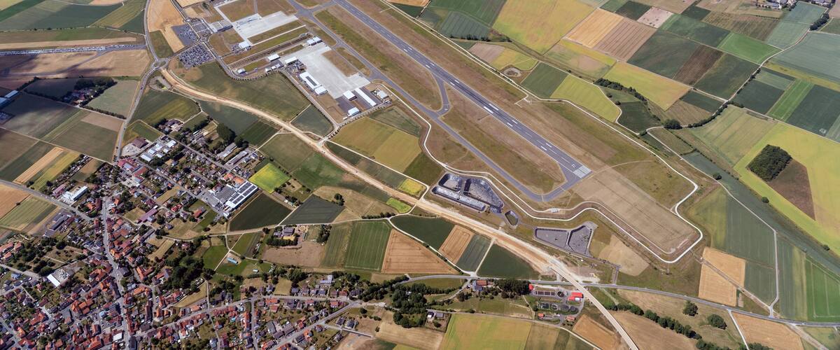 An aerial view of a rural area with a large open field, a small village, and a road network.