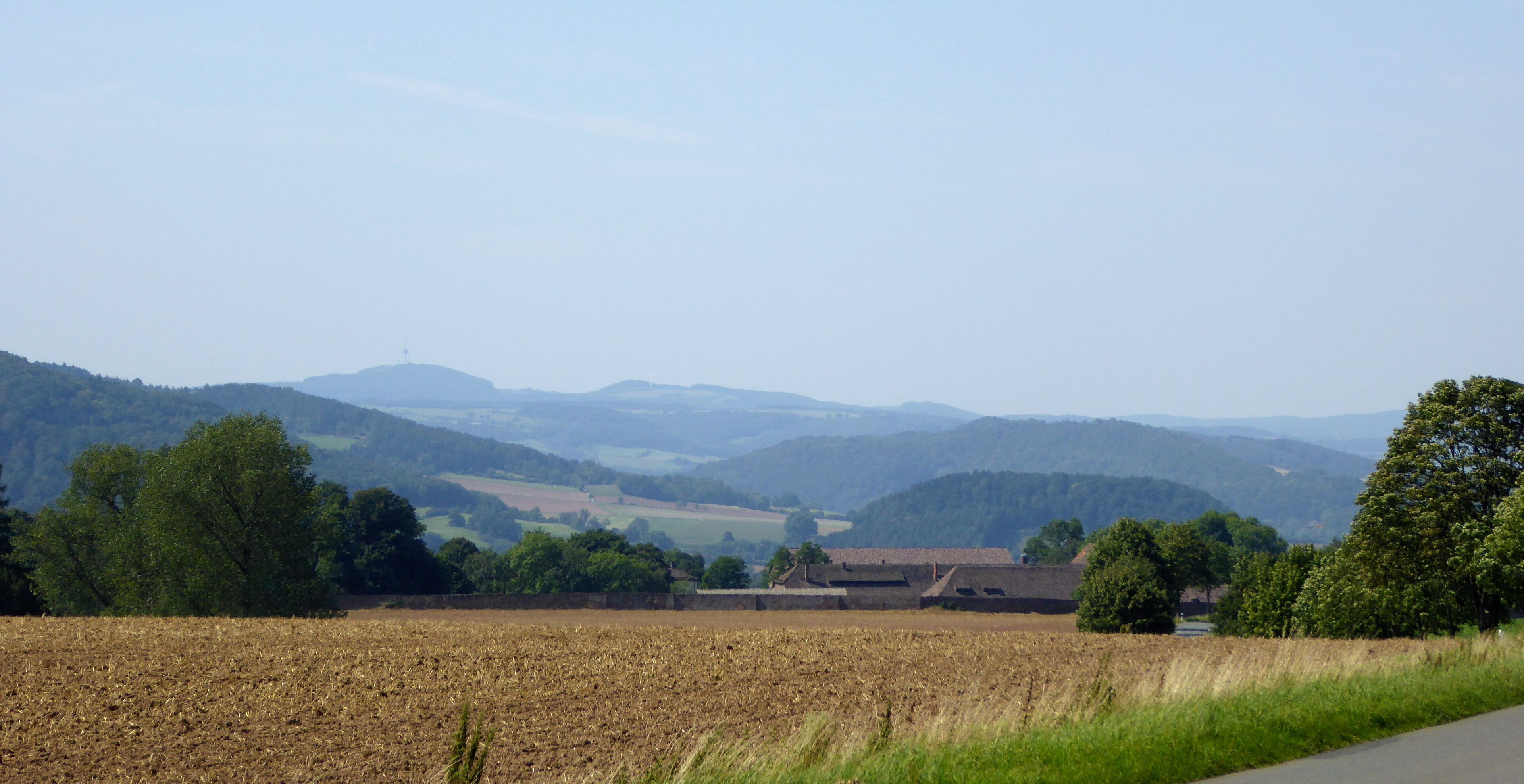 A rural landscape with a field, trees, and distant hills.