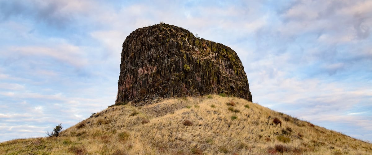A large rock formation on a grassy hill with a partly cloudy sky.