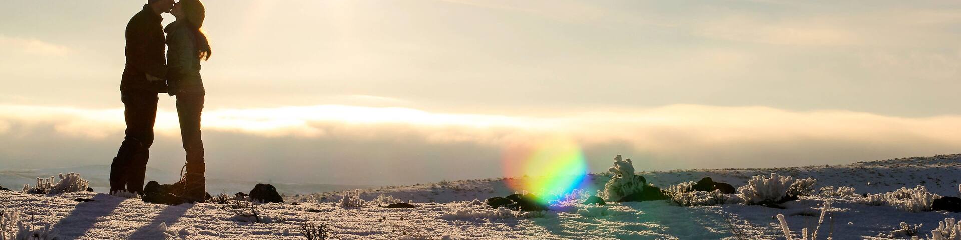 A young married couple kisses on top of a snowy mountain
