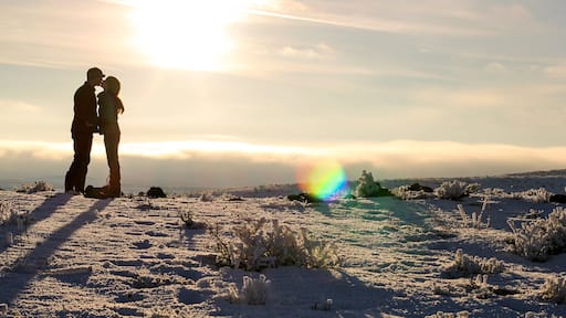 A young married couple kisses on top of a snowy mountain