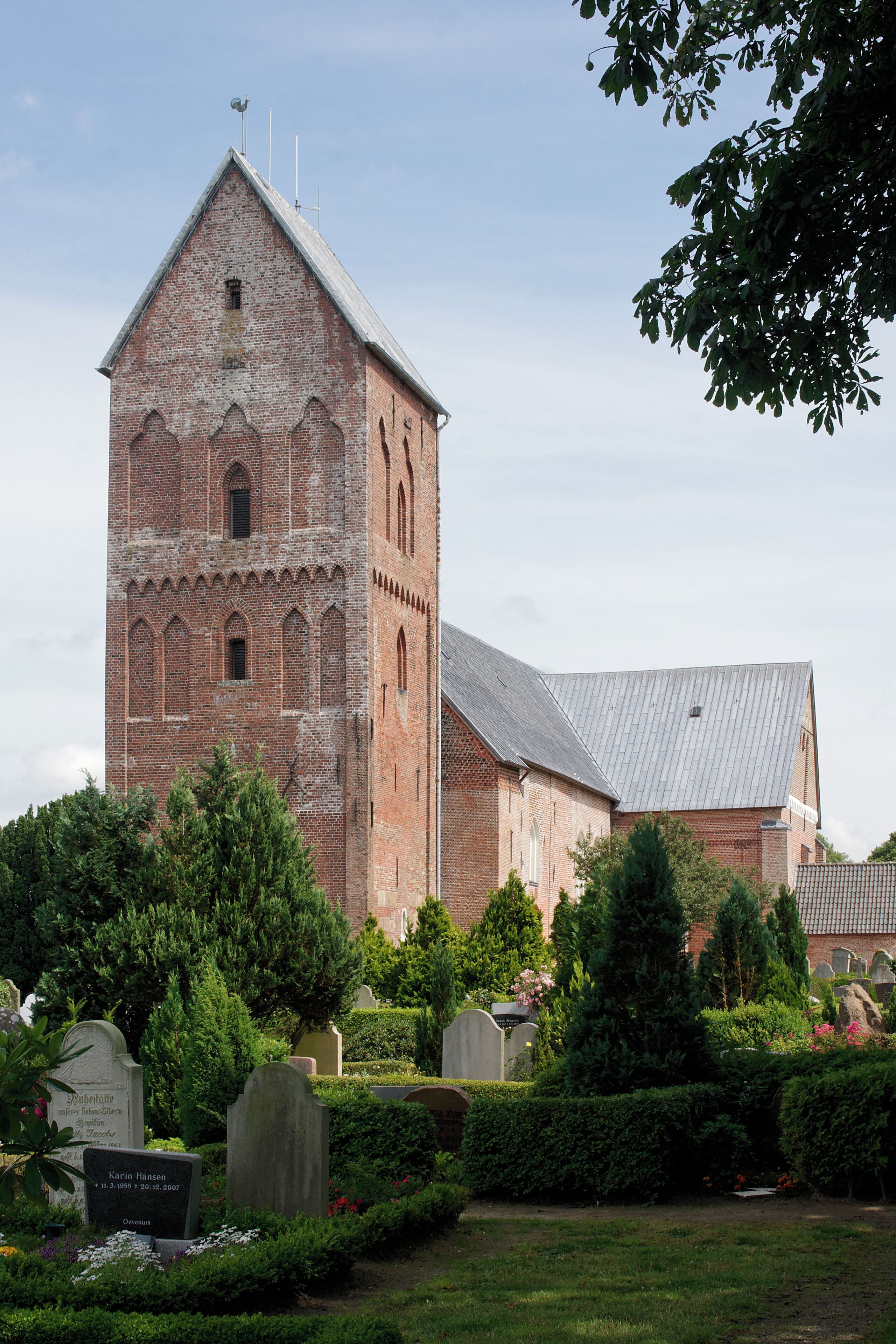 A historic brick church with a tall bell tower, surrounded by well-maintained hedges and a cemetery.
