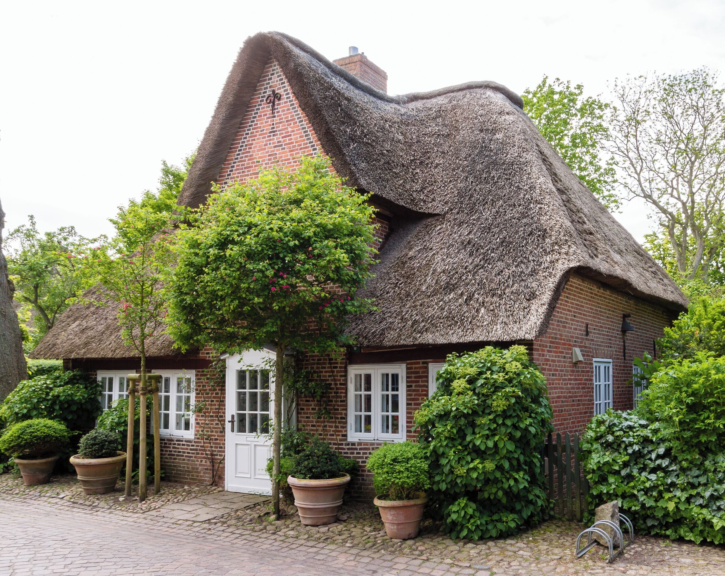 A thatched-roof house with brick walls, surrounded by potted plants and trees.