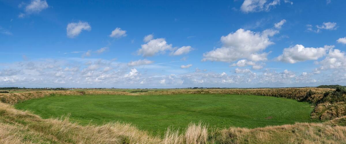 A green field with a clear sky and scattered clouds.