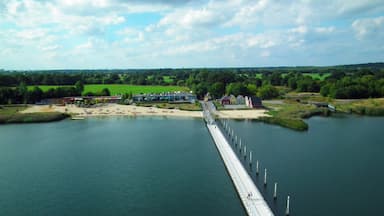Uma longa ponte sobre um rio, com edifícios e vegetação ao fundo.