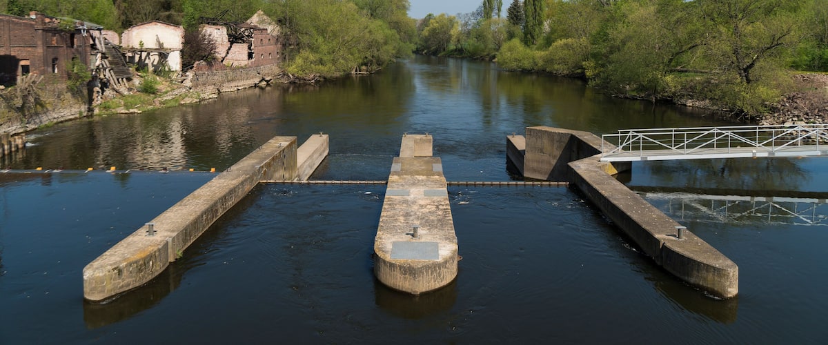 A lock system on a river with surrounding greenery and old buildings.