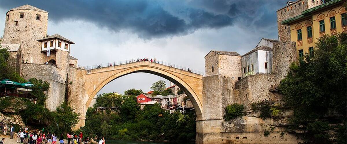 A stone bridge over a river, surrounded by historic buildings and a castle.
