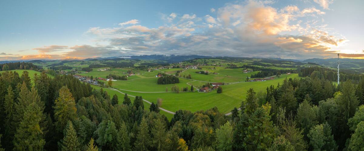 A panoramic view of a rural landscape with rolling hills, a winding road, and scattered houses.