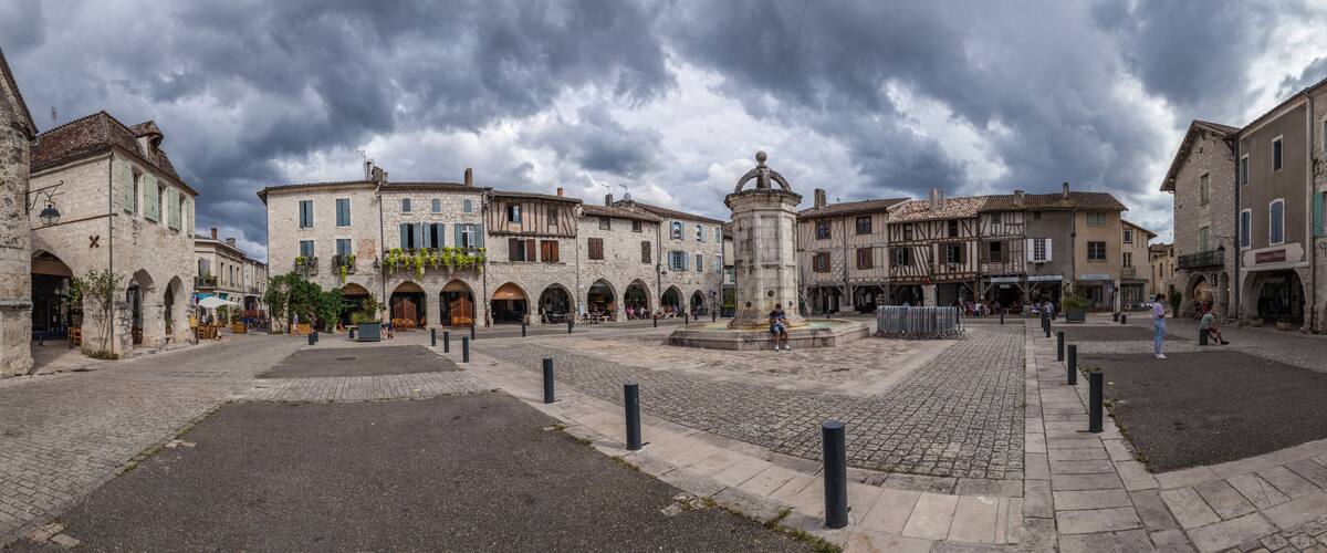 A historic square with cobblestone streets, stone buildings, and a central fountain.