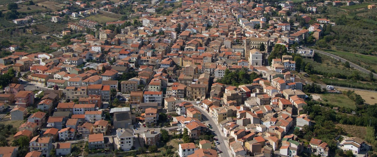 A densely packed town with red-roofed buildings, surrounded by rolling hills and distant mountains.