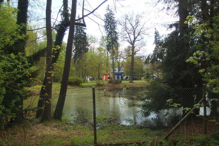 A pond surrounded by trees, a fence, and a small building in the background.
