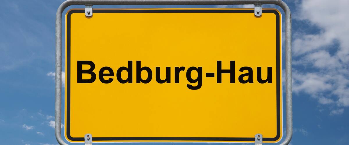 A yellow sign with the text "Bedburg-Hau" against a blue sky with clouds.