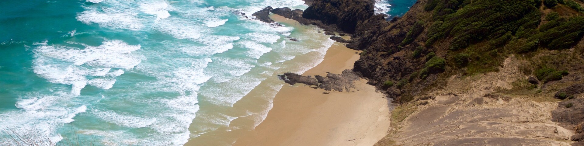Un paisaje costero con una playa arenosa, acantilados rocosos y olas del océano.