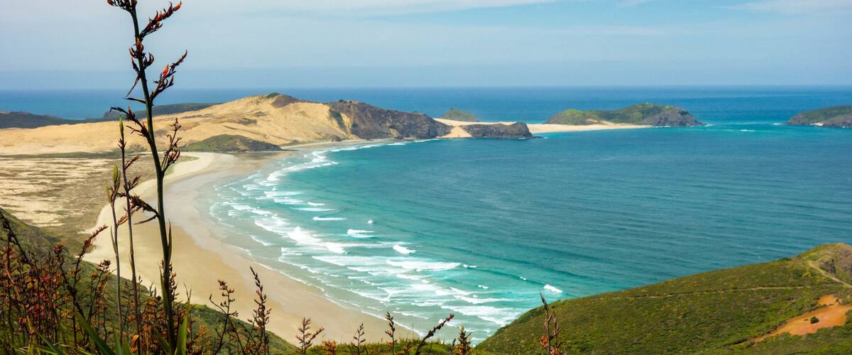 A coastal landscape with a sandy beach, green hills, and a clear blue ocean.