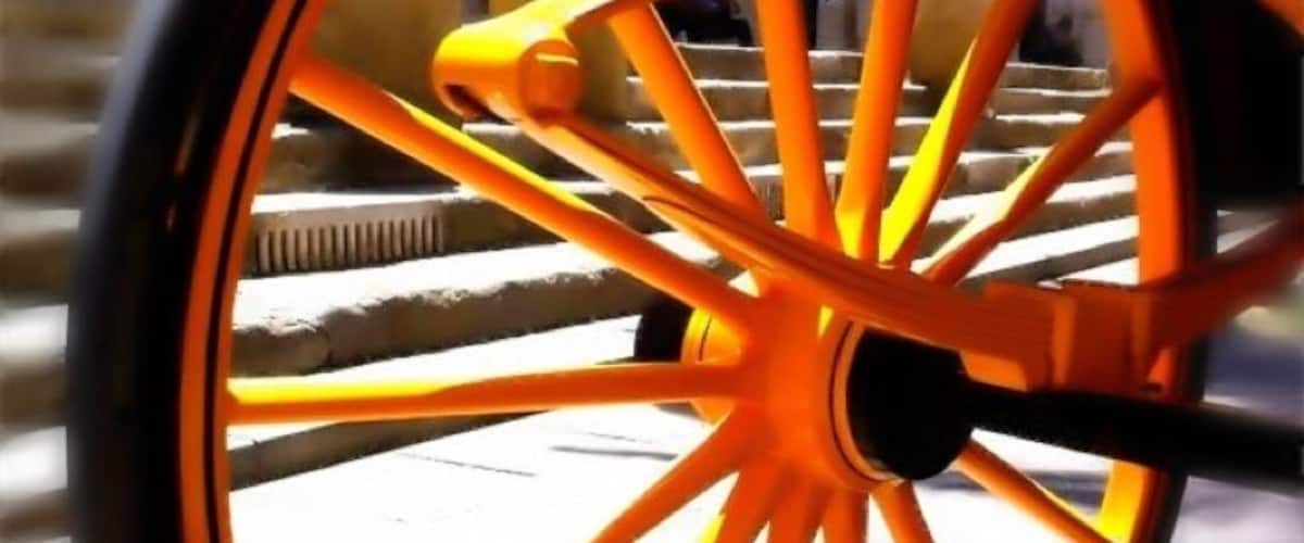 A close-up of a yellow bicycle wheel with a black tire, set against a blurred background of a staircase.