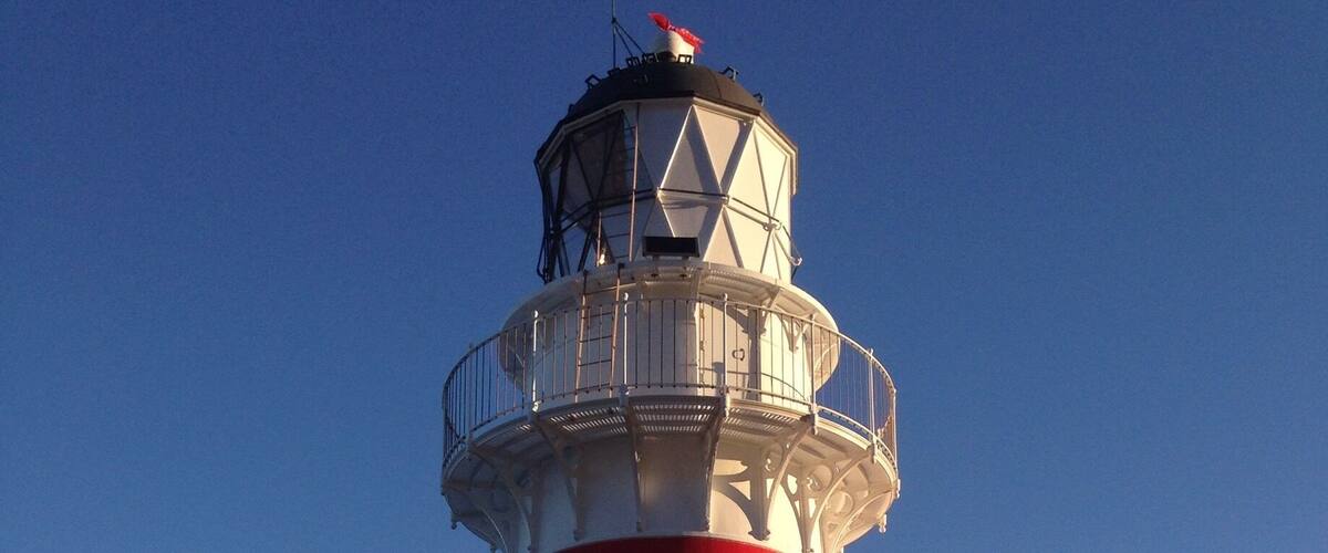 A red and white lighthouse with a metal railing and a door at the base, overlooking the ocean.