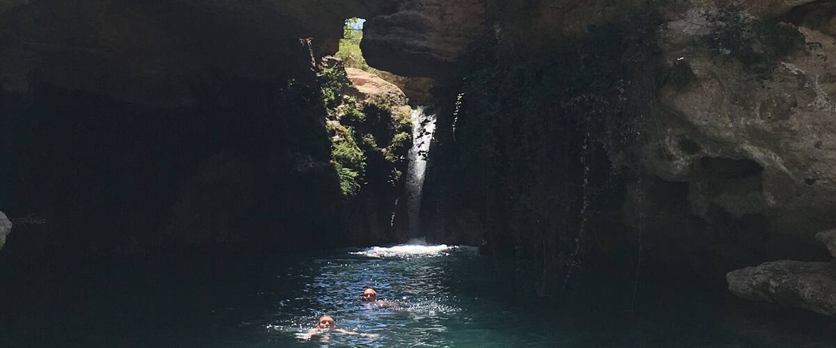 A natural rock formation with a clear water pool and a waterfall.