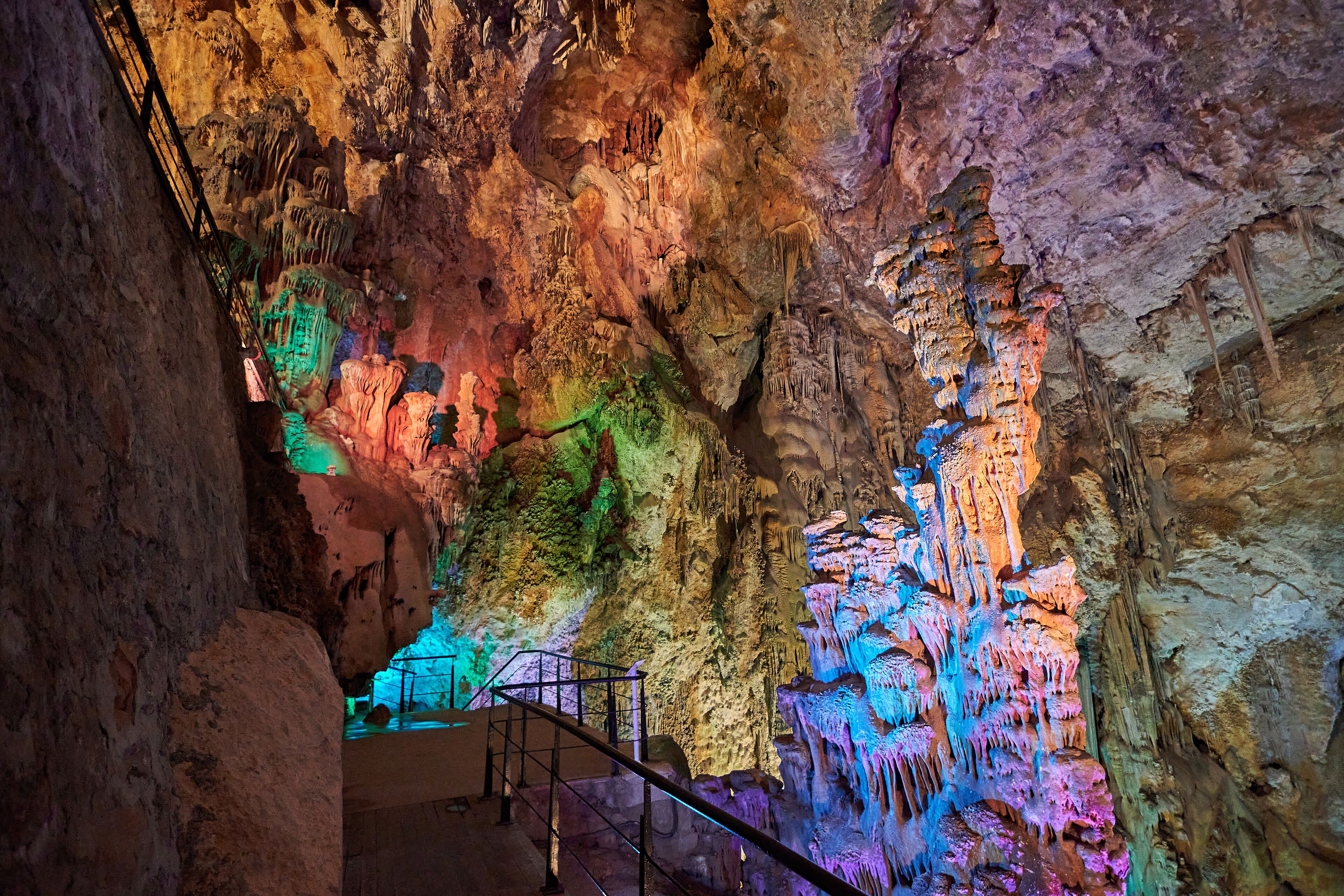 Caverna com estalactites e estalagmites coloridas iluminadas por iluminação artificial.