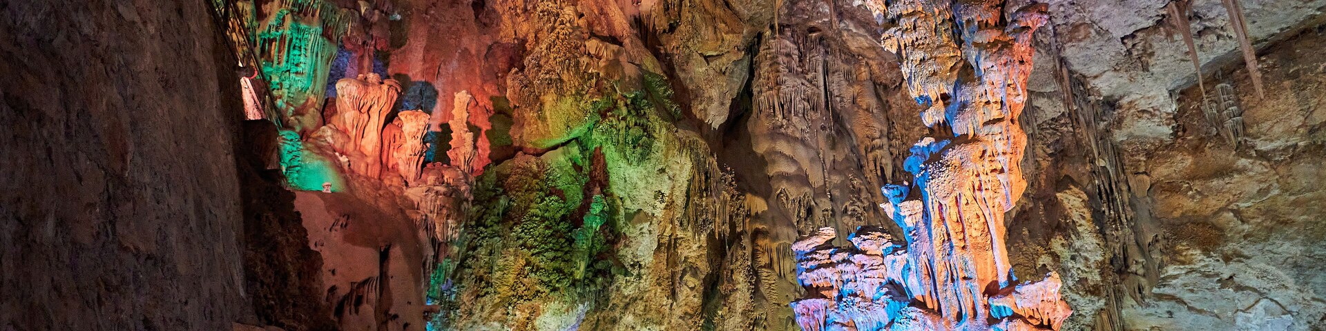 Caverna com estalactites e estalagmites coloridas iluminadas por iluminação artificial.