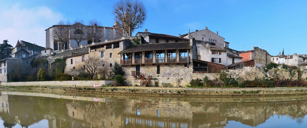 A historic town with stone buildings, a bridge, and a calm river reflecting the architecture.