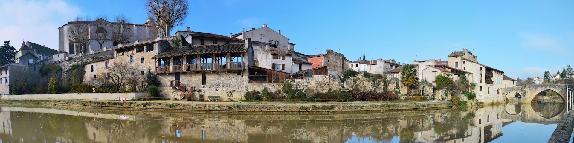 A historic town with stone buildings, a bridge, and a calm river reflecting the architecture.